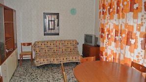Ein Wohnzimmer mit einem gemusterten Sofa, einem Holztisch und einem Fernseher auf einer Holzkommode.
