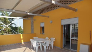 An outdoor patio with a round table and white chairs, a sliding glass door, and a tiled floor. - Felice C L in Bibione (San Michele al Tagliamento)