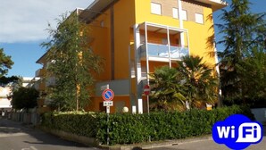A yellow building with a balcony, trees, and a no parking sign. - Felice C L in Bibione (San Michele al Tagliamento)