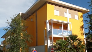 A yellow building with a balcony, a no parking sign, and a sign indicating a 24-hour area. - Felice CPT in Bibione (San Michele al Tagliamento)