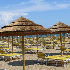 A beach with rows of yellow lounge chairs and thatched umbrellas. - Felice CPT in Bibione (San Michele al Tagliamento)