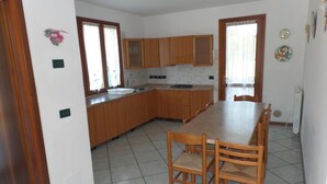 Une cuisine avec des meubles de rangement en bois, une table à manger avec des chaises et un sol carrelé.