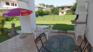 Une terrasse avec une table ronde et des chaises, une fontaine en pierre et un parasol rouge portant l’inscription « ALBIDA ».