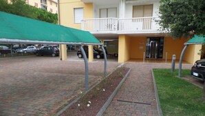 A parking area with cars, a green awning, and a building with a balcony.