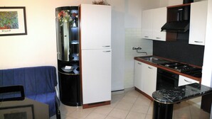 A compact kitchen with a refrigerator, stove, sink, and a blue sofa in the living area.