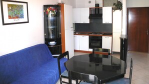 A compact living space with a kitchenette, a dining table with chairs, a blue sofa, and a framed picture on the wall.