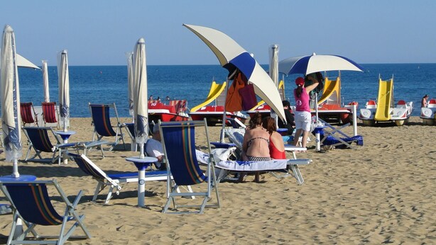 Une plage bordée de rangées de chaises longues et de parasols, dont certaines sont occupées.