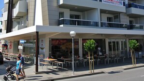 Un immeuble à plusieurs étages doté de balcons et d’un espace café situé au rez-de-chaussée.
