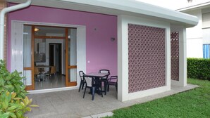 Ein modernes Haus mit rosafarbenem Anstrich, einer überdachten Terrasse mit Tisch und Stühlen sowie einem sichtbaren Küchenbereich.