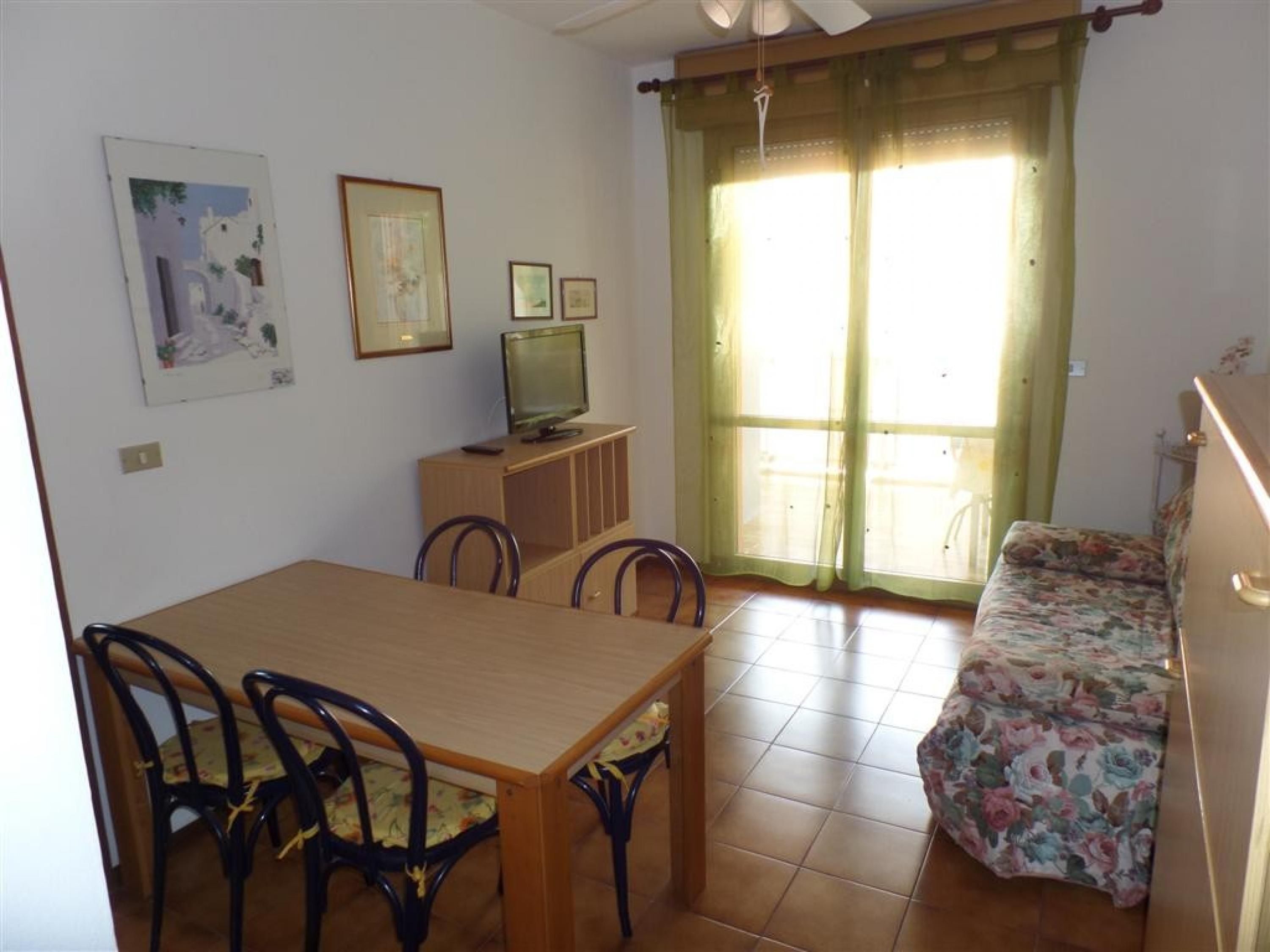 A dining area with a wooden table and chairs, a television on a cabinet, and a sofa with a floral cover.