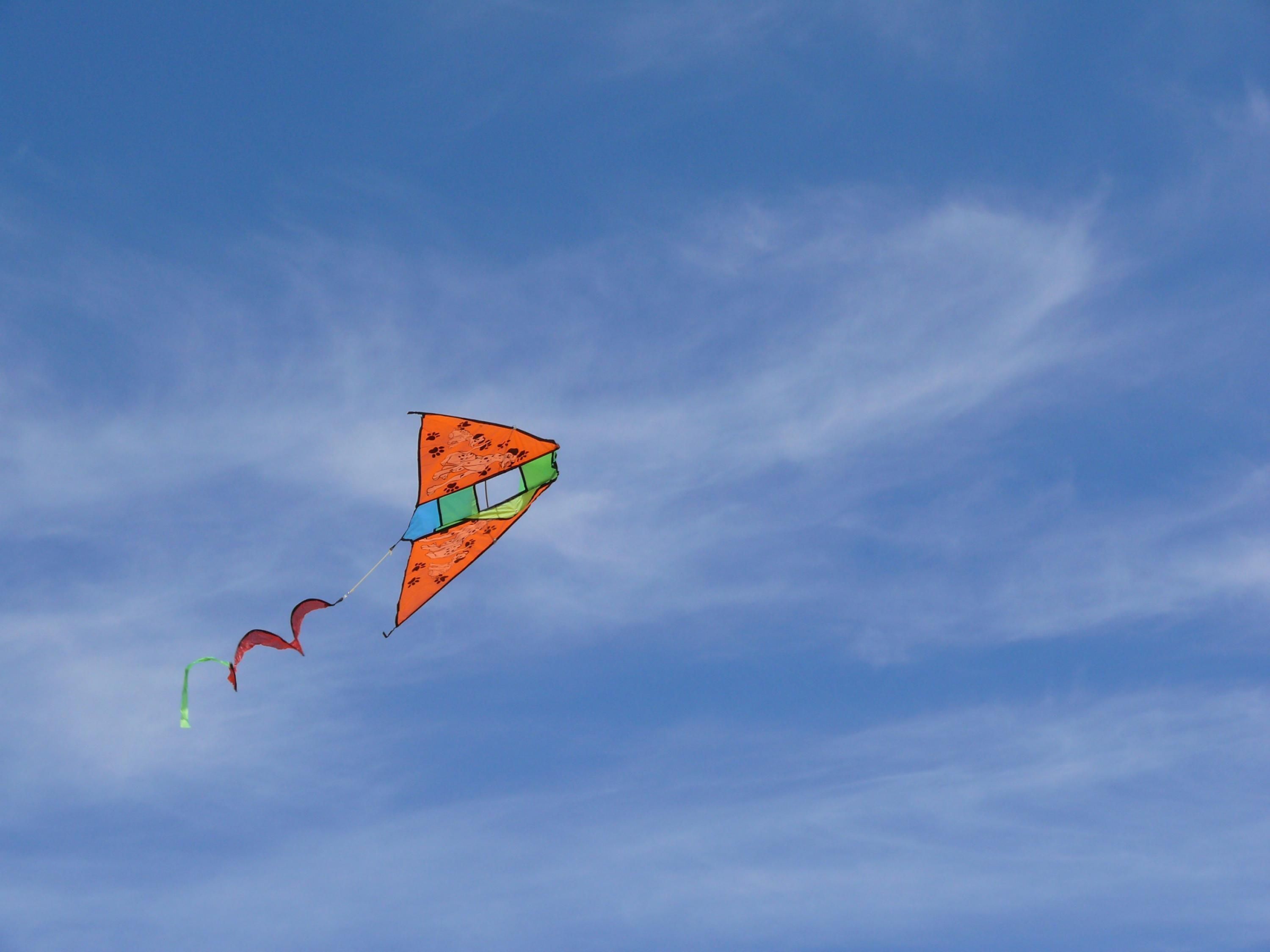 A kite with a triangular shape and a colorful design flying in the sky.