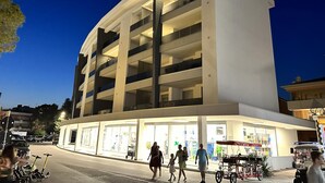 A modern multi-story building with a curved facade and illuminated ground floor. - Condominio Giardino B (San Michele al Tagliamento)