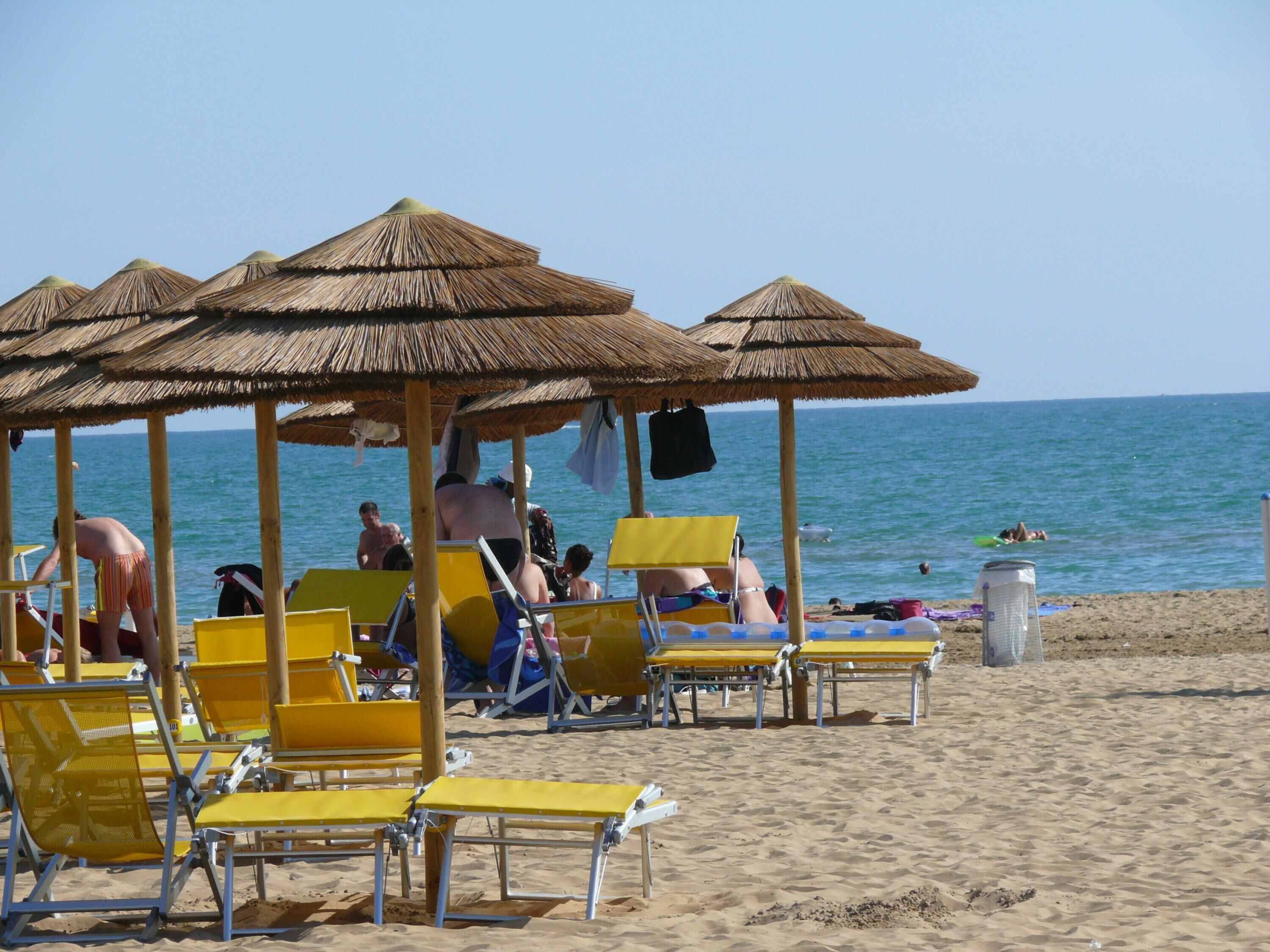 A beach with yellow lounge chairs and thatched umbrellas.
