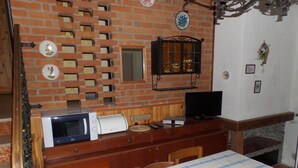 Eine Küche mit Ziegelwand, Mikrowelle, Toaster, Fernseher und einem Holztisch mit kariertem Tischläufer.