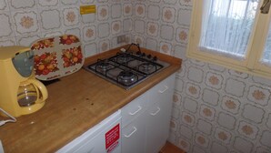 Eine kleine Küche mit einem Gaskochfeld, einem gelben Gerät und gemusterten Fliesen.
