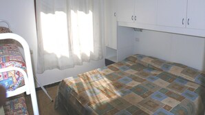 A small, simple room with a bed, a chair, and a wardrobe. - Holiday B A in Bibione (San Michele al Tagliamento)
