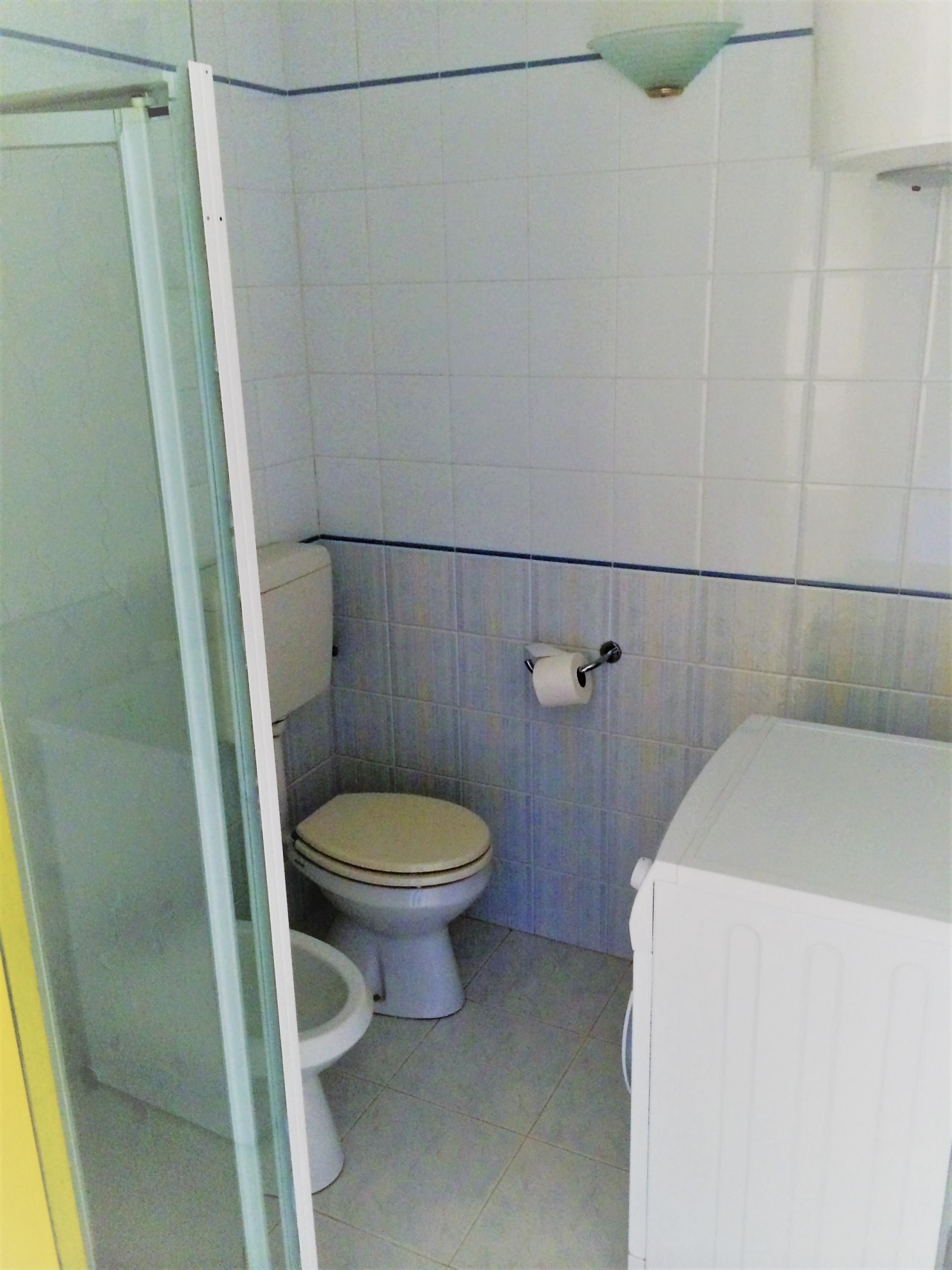 A small, compact bathroom with a toilet, a shower enclosure, and a sink.