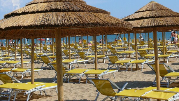 Une plage bordée de rangées de chaises longues jaunes et d’ombrelles en chaume.