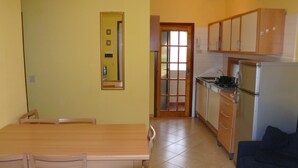 A compact kitchen with wooden cabinets, a dining table with chairs, and a dark-colored sofa.