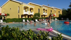 Ein Poolbereich mit Liegestühlen und Sonnenschirmen, umgeben von einem gelben Gebäude mit Balkonen.