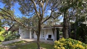 A white building with a covered patio area, surrounded by greenery and a stone pathway. - Villa Angi in Bibione (San Michele al Tagliamento)