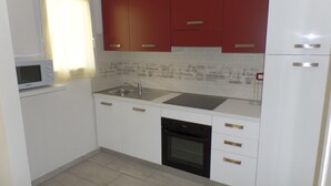 A compact kitchen with white cabinets, a microwave, a sink, and a dishwasher. - Villa Angi in Bibione (San Michele al Tagliamento)