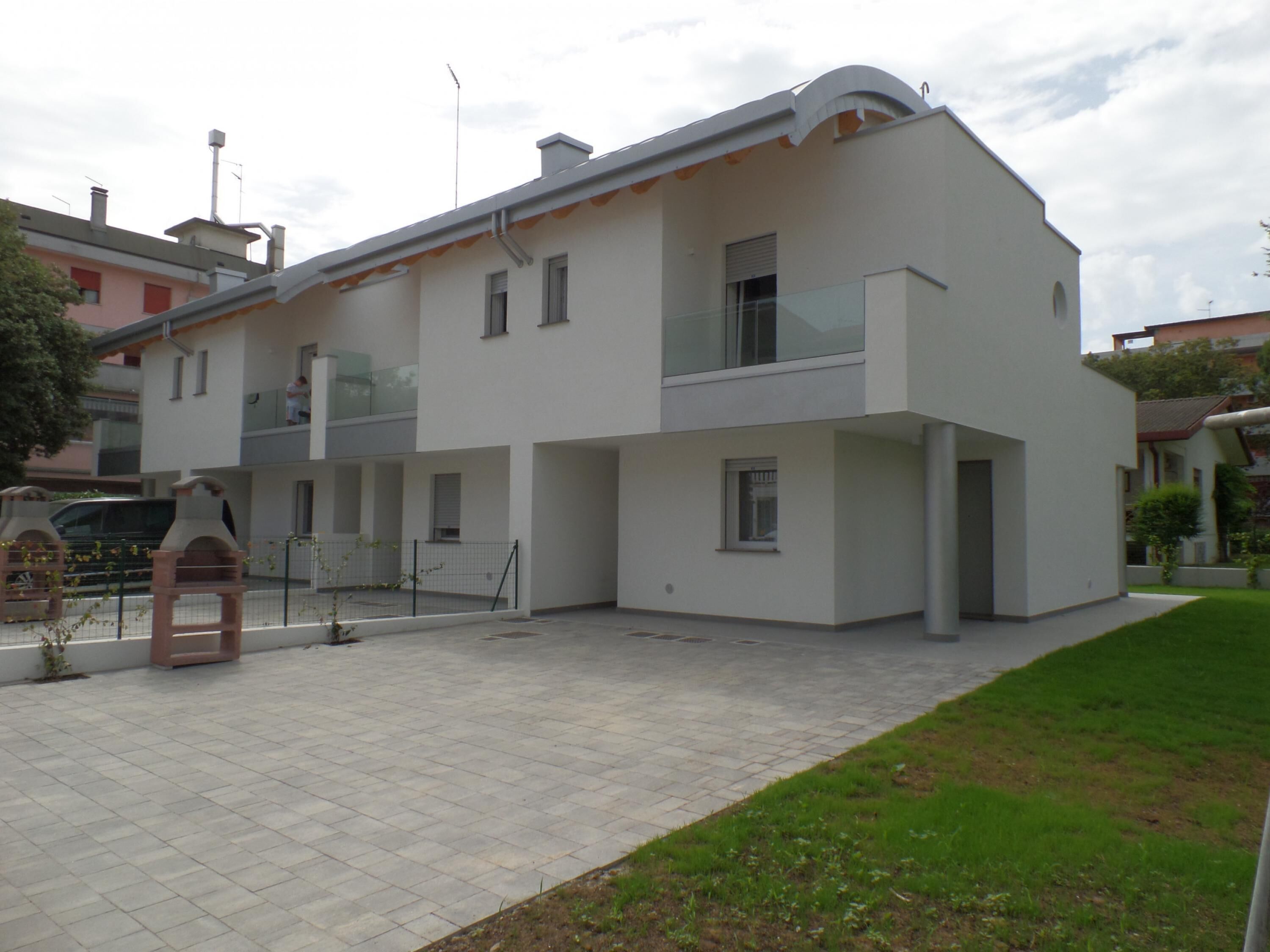 A modern two-story building with a flat roof, large windows, and a balcony.
