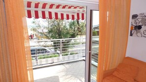 A balcony with a white railing, a red and white awning, and a view of parked cars and trees.