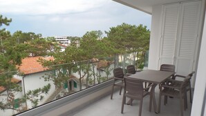 A balcony with a table and chairs, overlooking a residential area with trees and buildings. - Melograno C Mans in Bibione (San Michele al Tagliamento)