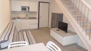 A compact kitchen with a microwave, refrigerator, and a dining area with a table and chairs. - Melograno C Mans in Bibione (San Michele al Tagliamento)