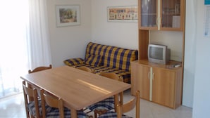 A compact living space with a wooden dining table, a sofa, and a television on a cabinet. - Holiday 5 in Bibione (San Michele al Tagliamento)