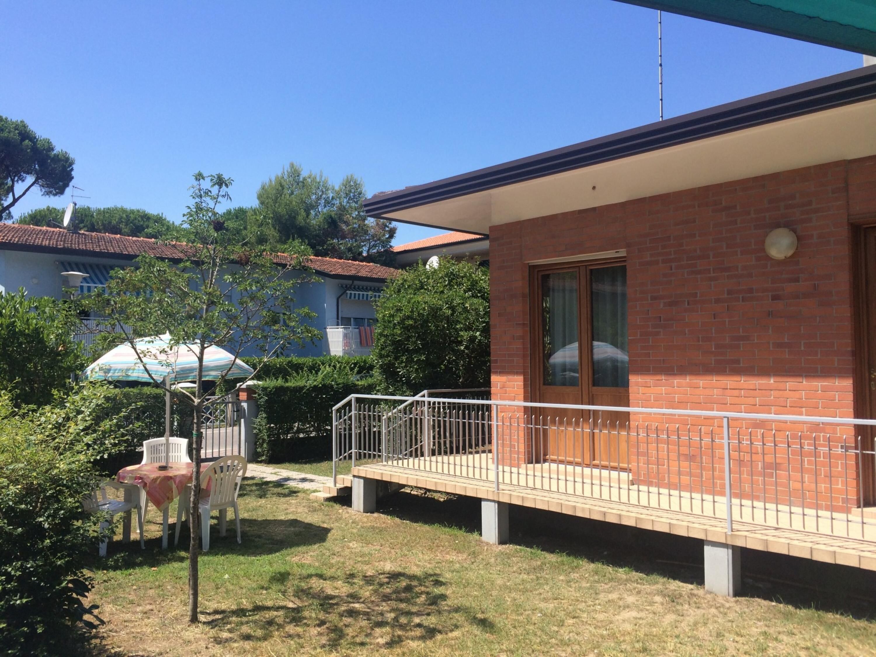 Um edifício residencial com fachada de tijolos, uma varanda com guarda-corpo de metal e uma pequena área de pátio com mesa e cadeiras.