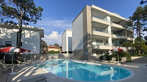 A modern building with a swimming pool, surrounded by lounge chairs and umbrellas. - Melograno A C2 in Bibione (San Michele al Tagliamento)