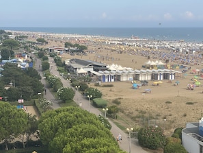 A beach with numerous tents and beach umbrellas, a paved walkway, and a view of the sea.
