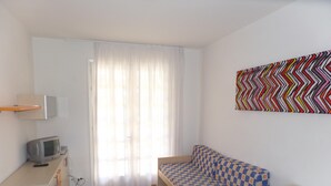 A small, bright room with a checkered sofa, a television on a cabinet, and a colorful zigzag wall art piece.