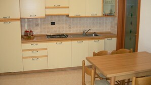 A kitchen with beige cabinets, a wooden countertop, a sink, and a dining table with chairs. - LIA Pool in Bibione With 1 Bedrooms and 1 Bathrooms (San Michele al Tagliamento)