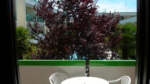 A balcony with a round table and four chairs, a tree with red leaves, and a building in the background. - LIA Pool in Bibione With 1 Bedrooms and 1 Bathrooms (San Michele al Tagliamento)