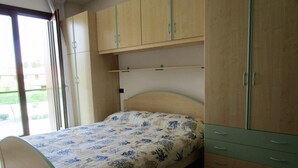 A bedroom with a bed, wooden cabinets, and a window. - LIA Pool in Bibione With 1 Bedrooms and 1 Bathrooms (San Michele al Tagliamento)