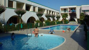 A swimming pool area with a building in the background. - LIA Pool in Bibione With 1 Bedrooms and 1 Bathrooms (San Michele al Tagliamento)