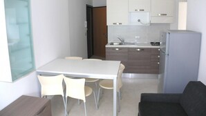 A compact kitchen with a dining area, a refrigerator, and a glass partition. - Roby 6 in Bibione With 2 Bedrooms and 1 Bathrooms (San Michele al Tagliamento)