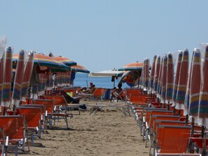 A beach with rows of orange beach chairs and umbrellas. - Bristol 115 in Bibione (San Michele al Tagliamento)