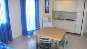 A compact kitchen with white cabinets, a microwave, and a sink. There is a dining table with chairs in the foreground. - Horizon 16 in Bibione (San Michele al Tagliamento)