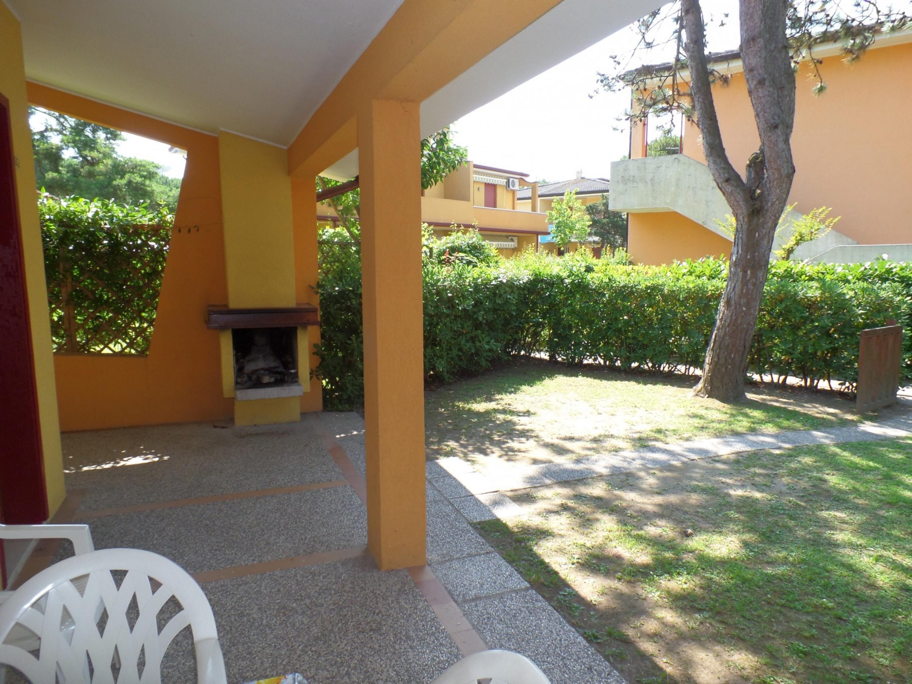 An outdoor patio area with a fire pit, yellow walls, and a view of a building in the background.