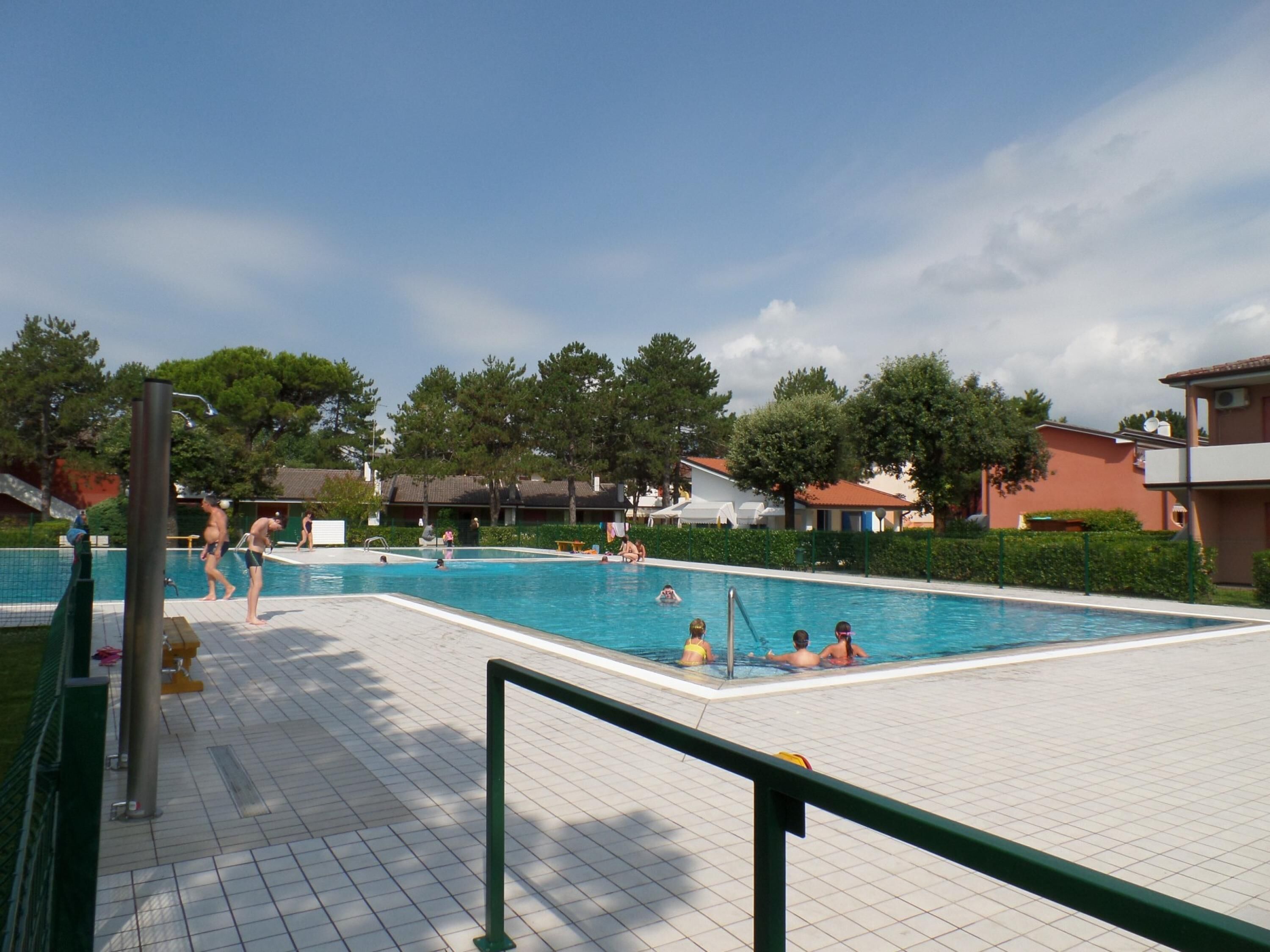 A swimming pool with people in the water, surrounded by buildings and trees.