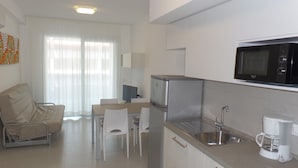 A compact kitchen with a microwave, refrigerator, and sink. There is a dining area with a table and chairs. - Polaris B in Bibione (San Michele al Tagliamento)