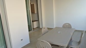 A dining area with a table and chairs, a small window, and a door leading to a kitchen. - Polaris B in Bibione (San Michele al Tagliamento)