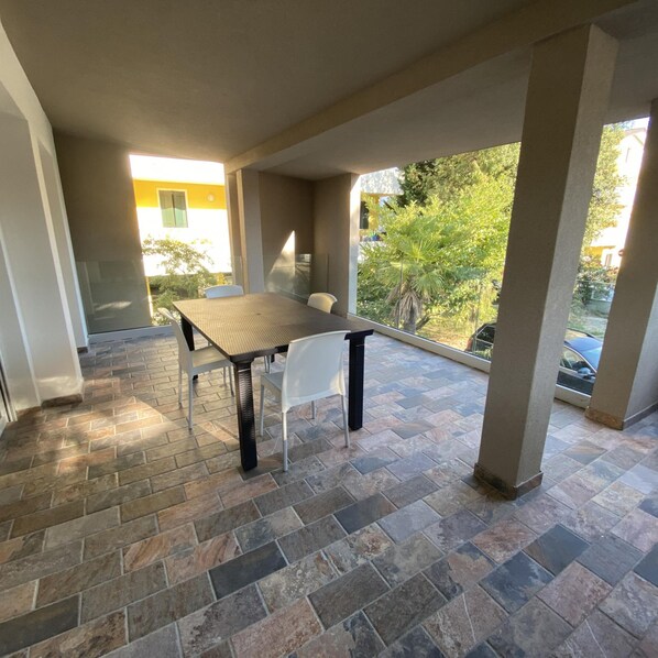 Un espace extérieur aménagé en terrasse, avec une table et des chaises, un sol en pierre et une vue sur la verdure et les bâtiments.