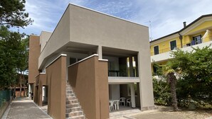 Ein modernes Gebäude mit flachem Dach, einer Treppe zu einer oberen Ebene und einer Terrasse mit Außenmöbeln.
