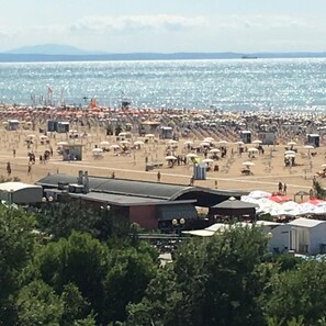 Une plage avec de nombreux parasols et beaucoup de monde, quelques bâtiments au premier plan, et une vue dégagée sur la mer.