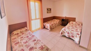 Een kamer met drie bedden, een raam met gordijnen, een klein tafeltje en een plafondlamp.